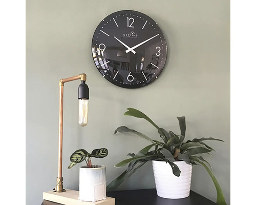 Scenă decorativă cu un ceas de perete negru, o lampă de masă din cupru și două plante de interior în ghivece.