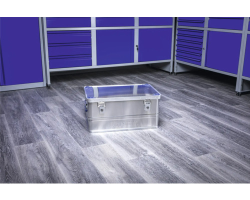 Cutie de scule din aluminiu pe o podea de atelier în fața dulapurilor de scule albastre