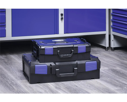 Două cutii de scule din plastic stivuite în fața unui banc de lucru