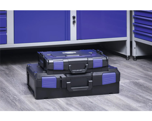 Două cutii de scule de dimensiuni diferite, stivuite în fața unui dulap de atelier.