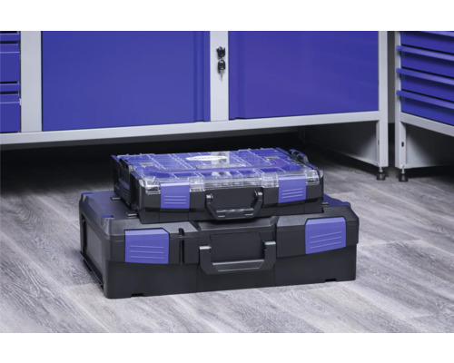 Două cutii de scule din plastic stivuite în fața unui dulap de atelier