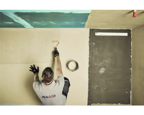 Un bărbat aplică vopsea lavabilă pe un perete cu trafaletul