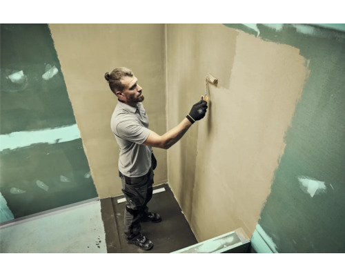 Un bărbat vopsește un perete cu trafaletul într-o baie