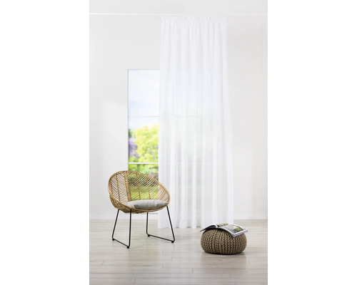 Cameră luminoasă cu perdea albă, fotoliu din ratan și puf cu revistă