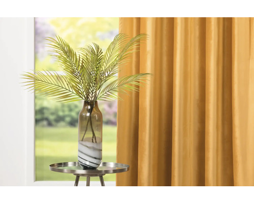 Plantă artificială decorativă într-un vas de sticlă pe o măsuță laterală în fața unei ferestre cu perdea.