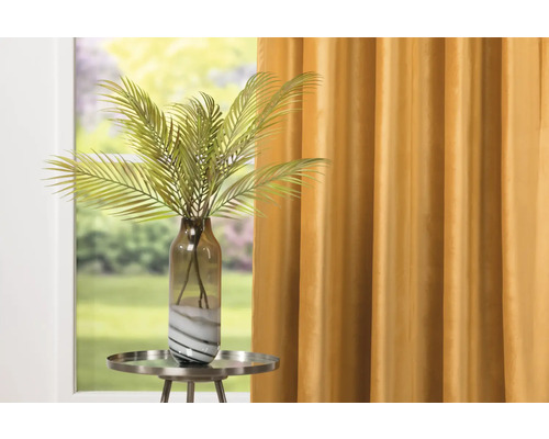 Plantă artificială decorativă cu palmier în vază de sticlă pe o măsuță laterală în fața unei perdele