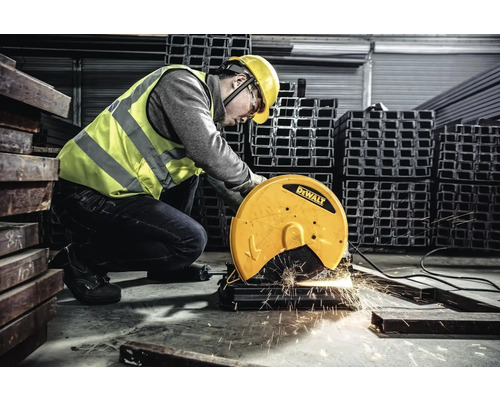 Un muncitor cu cască de protecție și vestă de siguranță operează un ferăstrău metalic DeWalt într-un atelier.