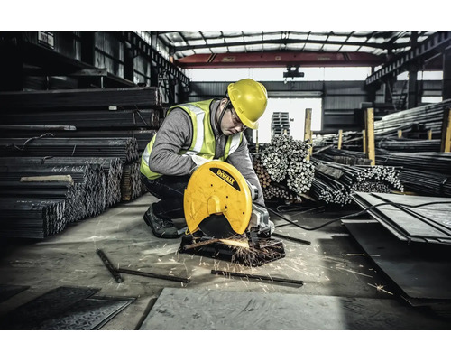 Un muncitor cu cască de protecție și vestă de siguranță taie metal cu o mașină de debitat într-o hală de fabrică.