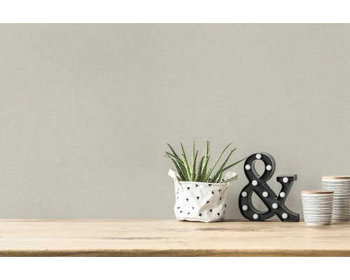 Scenă de locuit luminoasă cu tapet textil, plantă, obiect decorativ și recipiente pe o masă de lemn.