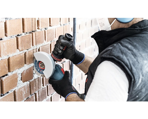 Artizan care taie un zid de cărămidă cu un polizor unghiular.