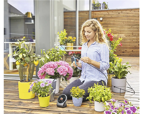 Femeie tăind furtun de irigare pentru plante pe o terasă