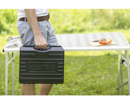 Persoană care transportă grătarul Campingaz într-o cutie de transport în grădină