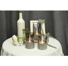 Scenă decorativă cu trei sfeșnice din sticlă și beton pe o masă