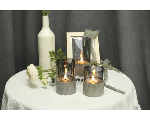 Scenă decorativă cu trei sfeșnice din sticlă și beton pe o masă