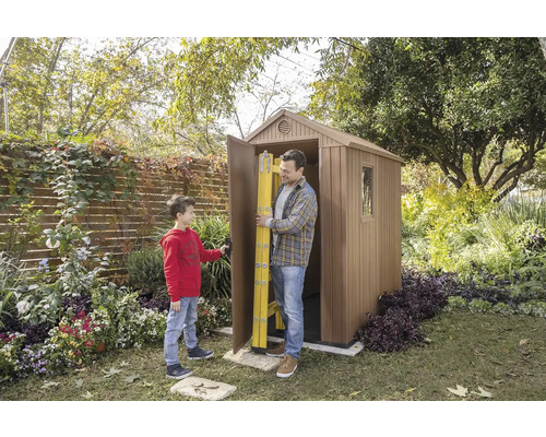 Un bărbat și un băiat în fața unei căsuțe de grădină cu o ușă deschisă în care se află o scară.