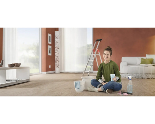 Femeie stă pe podea cu găleată și ustensile de curățenie în sufragerie