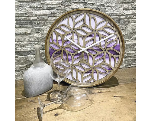 Ceas decorativ din lemn cu model filigran de frunze lângă două pahare de vin și o sticlă decorativă
