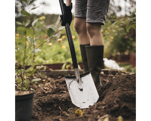 O persoană sapă în grădină cu o sapă.