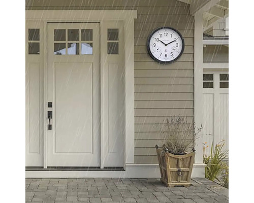 Scenă cu un ceas rotund de exterior rezistent la intemperii lângă o ușă de intrare în timpul unei averse.