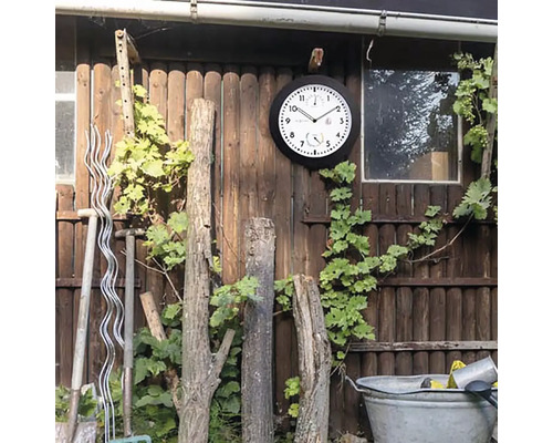 Scenă exterioară cu ceas de perete, viță de vie, unelte de grădinărit și gard din lemn