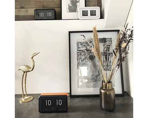 Scenă decorativă cu ceas cu clapetă, vază de flori, ramă foto și figurină pasăre.