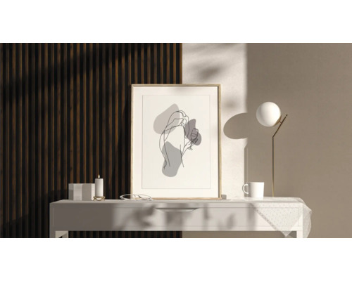 Imagine decorativă cu reprezentare abstractă a unei femei în ramă pe o masă cu lampă, ceașcă și lumânare