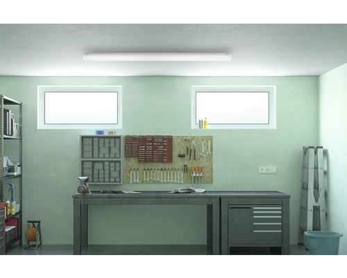 Atelier cu banc de lucru, panou pentru scule și rafturi sub o lampă de tavan.