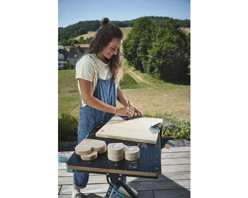Femeie care lucrează afară pe un banc de lucru cu lemn, un unghi pătrat și un creion.
