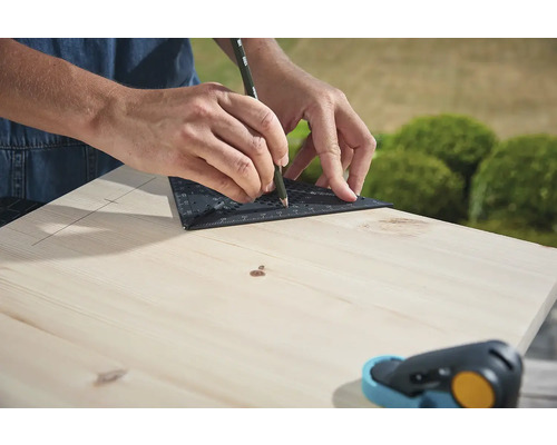 O persoană trasează o linie cu un raportor și un creion pe o scândură de lemn.