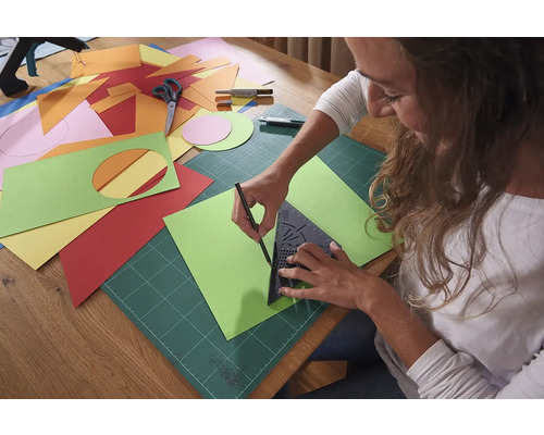 Femeie care desenează un șablon de hârtie verde cu un triunghi, un suport de tăiere și un creion.