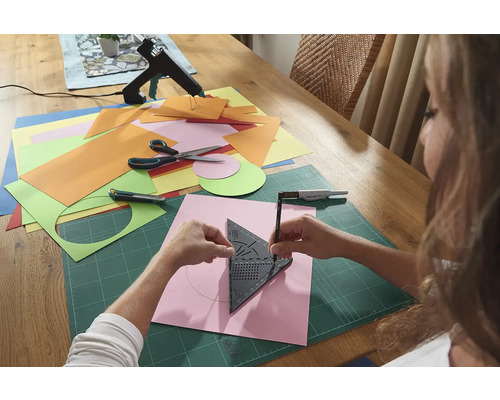 Femeie care desenează un cerc cu un echer pe o bucată de hârtie, înconjurată de materiale de artizanat pe o masă.