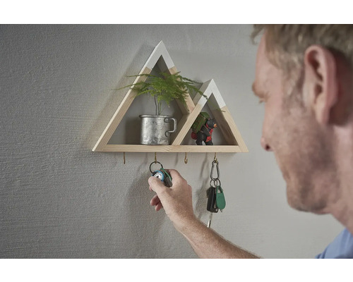 Raft decorativ de perete în formă de munte cu cârlige pentru chei și o persoană care agață un breloc