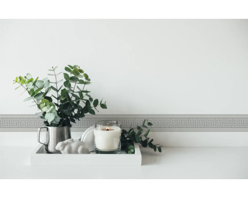 Bordură decorativă cu model meandru pe perete deasupra unei mese cu lumânare și plantă