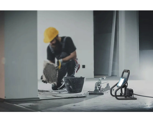 Artizan care pune gresie cu unelte și reflector de șantier