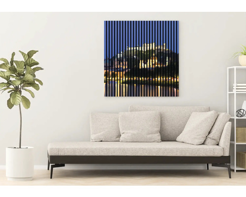 Artă decorativă de perete cu un motiv de peisaj urban în spatele unor linii verticale deasupra unei canapele într-un living.