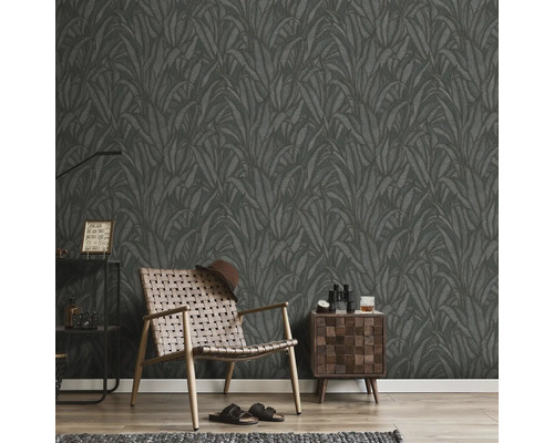 Cameră cu tapet închis cu motiv de frunze, fotoliu, noptieră și decorațiuni