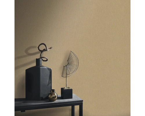 Scenă decorativă cu tapet texturat, completată de o vază neagră, o sferă aurie și o sculptură metalică în formă de evantai pe o masă.