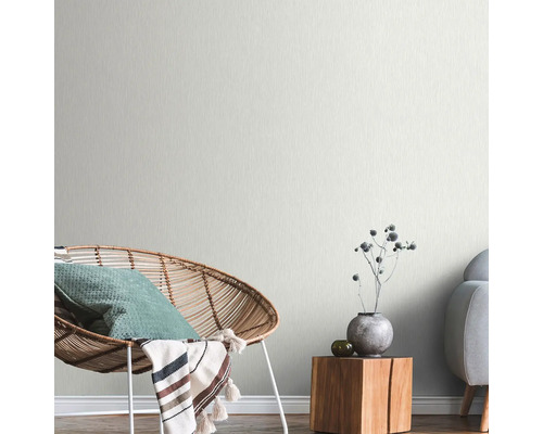 Cameră de zi luminoasă cu fotoliu din ratan, masă din lemn și tapet cu model subtil.