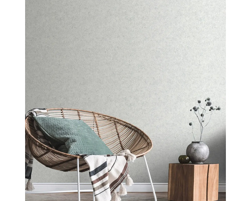 Cameră de zi cu fotoliu din ratan, pernă, pătură și măsuță laterală din lemn cu decorațiuni în fața unui tapet texturat