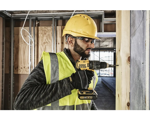 Un muncitor în construcții cu cască de protecție și ochelari de protecție folosește o șurubelniță cu acumulator DeWalt.