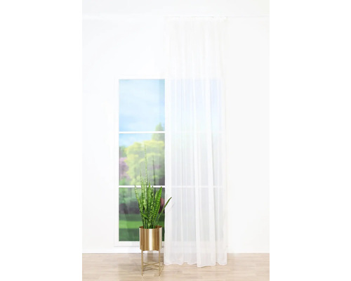 Plantă decorativă de interior într-un ghiveci auriu în fața unei ferestre cu perdea.