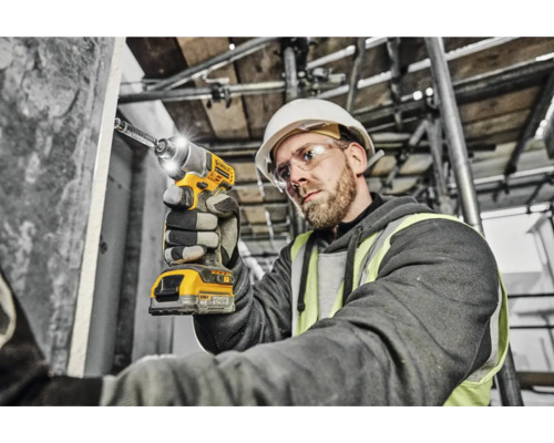 Un muncitor în construcții folosește o șurubelniță cu impact cu acumulator galbenă DeWalt pe un șantier.