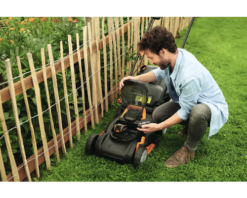 Bărbat schimbând bateria unei mașini de tuns iarba în grădină.