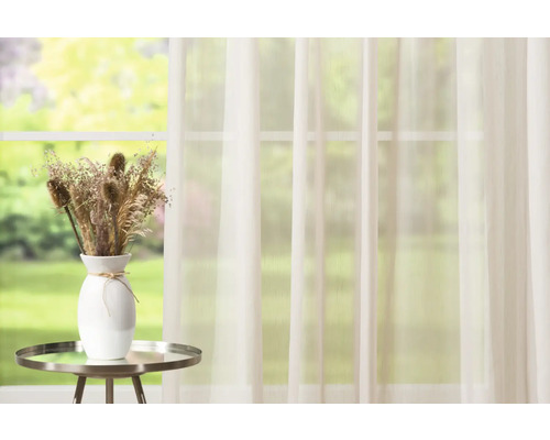 Scenă decorativă cu perdea, vază și flori uscate pe o masă în fața unei ferestre.