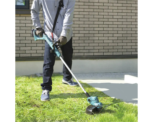 O persoană folosește o mașină de tuns iarba cu acumulator în grădină pentru a tunde iarba.