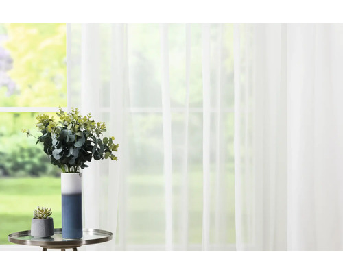 Atmosferă decorativă de locuit cu perdea, vază și plante artificiale pe o măsuță laterală în fața unei ferestre.