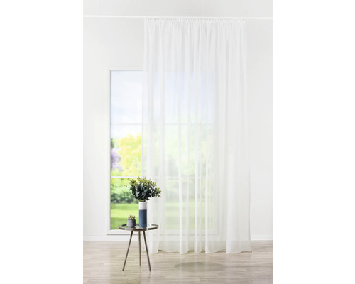 Cortină albă din voal în fața unei ferestre, completată de o masă cu o vază cu flori