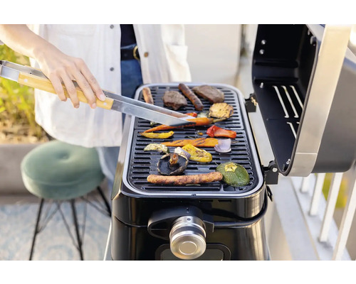 O persoană face grătar cu legume și carne pe un grătar.