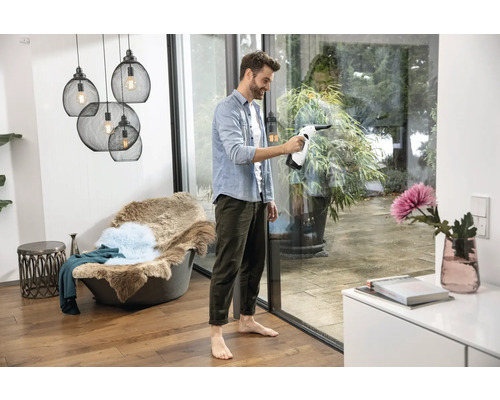 Un bărbat curăță ferestrele cu un aspirator de geamuri într-o cameră luminoasă