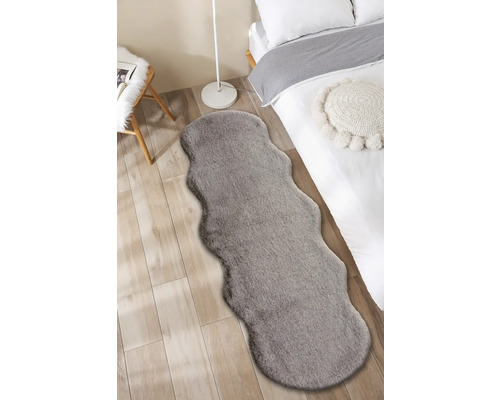 Fotografie de interior a unui dormitor cu un pat și un covor gri cu aspect de blană.